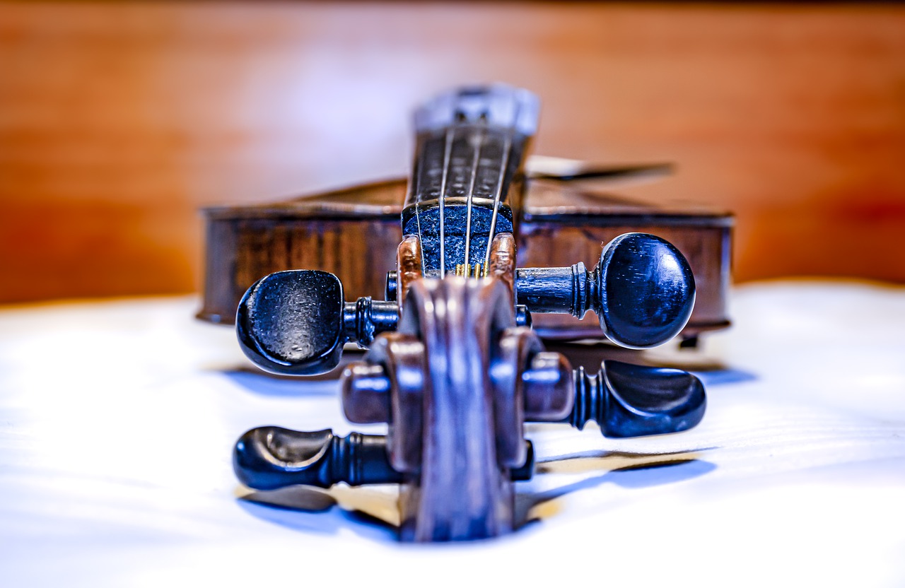 Image of a viola or violin on a table. It's an closeup image with the adjuster knobs and top of the neck of the instrument mostly filling the screen